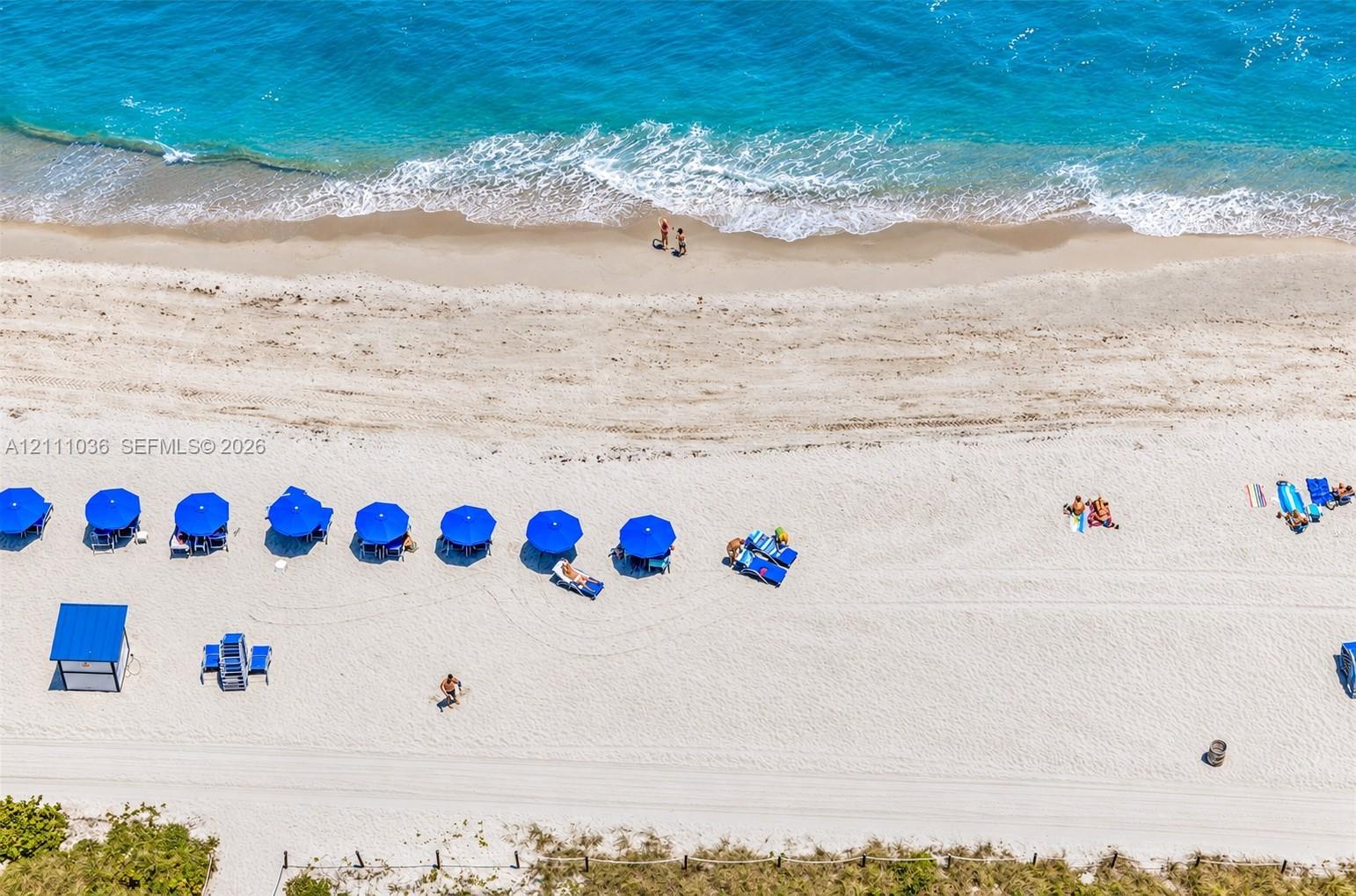 Direct oceanfront access featuring expansive sandy shoreline, turquoise water, and professional hardscaping