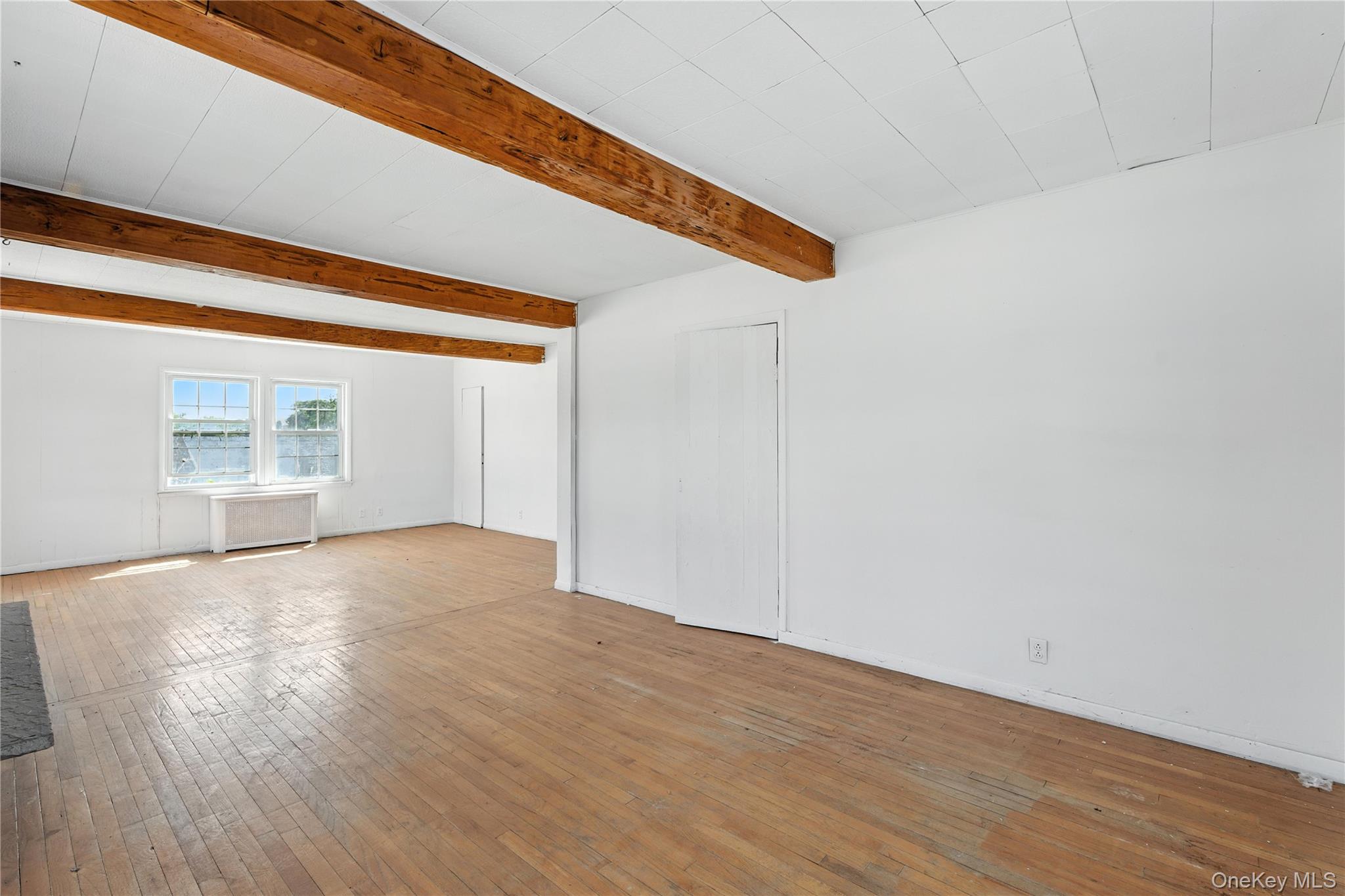Unfurnished living room featuring wood-type flooring, beamed ceiling, and radiator