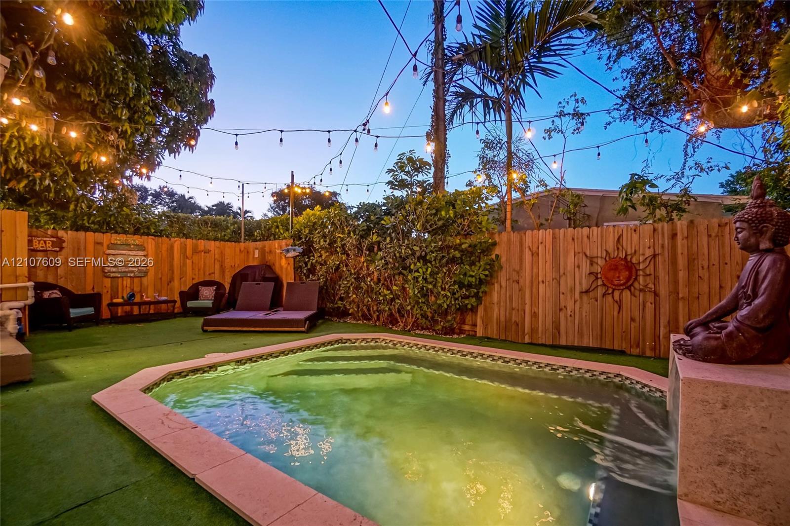 Backyard featuring a custom-shaped pool with integrated stairs, perimeter stone coping, vertical wood privacy fencing, and overhead string lighting