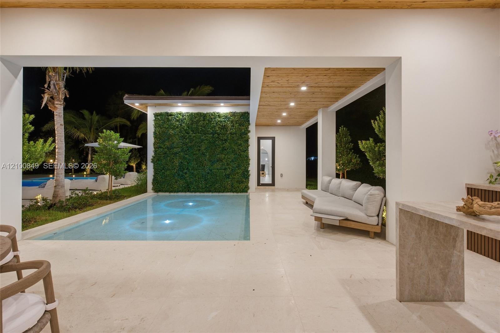 Covered terrace featuring light stone flooring, wood-paneled ceiling with recessed lighting, integrated swimming pool, and a vertical garden wall