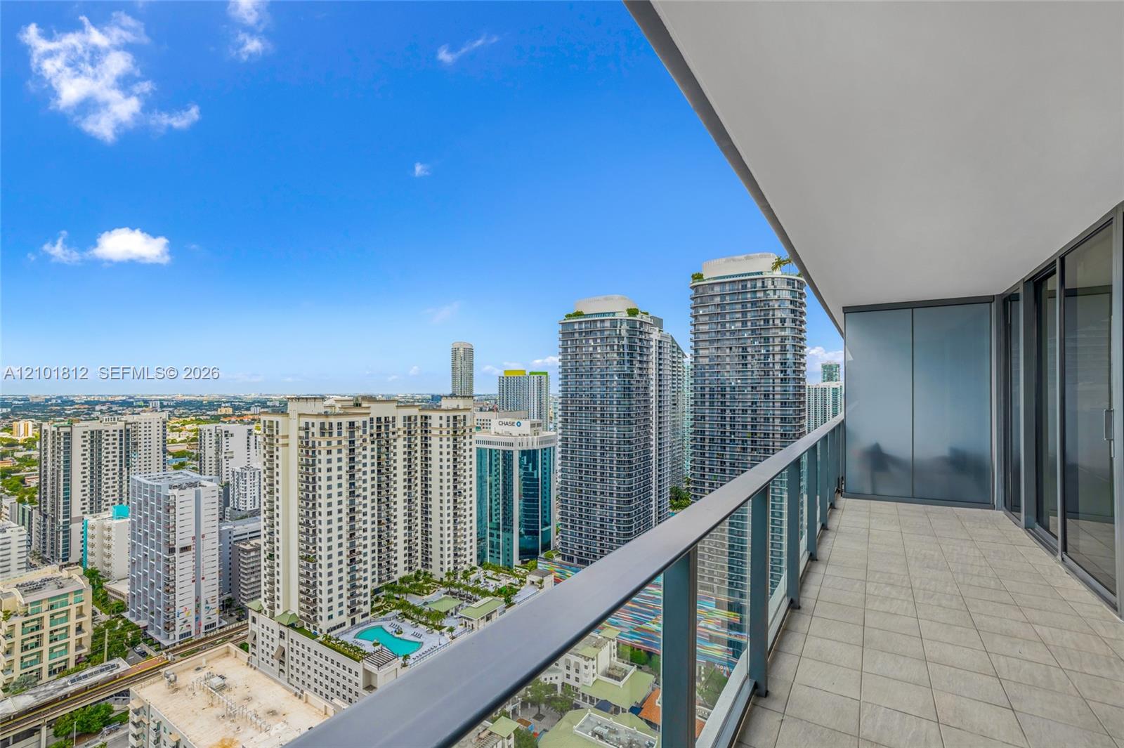 Covered private balcony with tile flooring, glass panel railing, and full-height sliding glass door