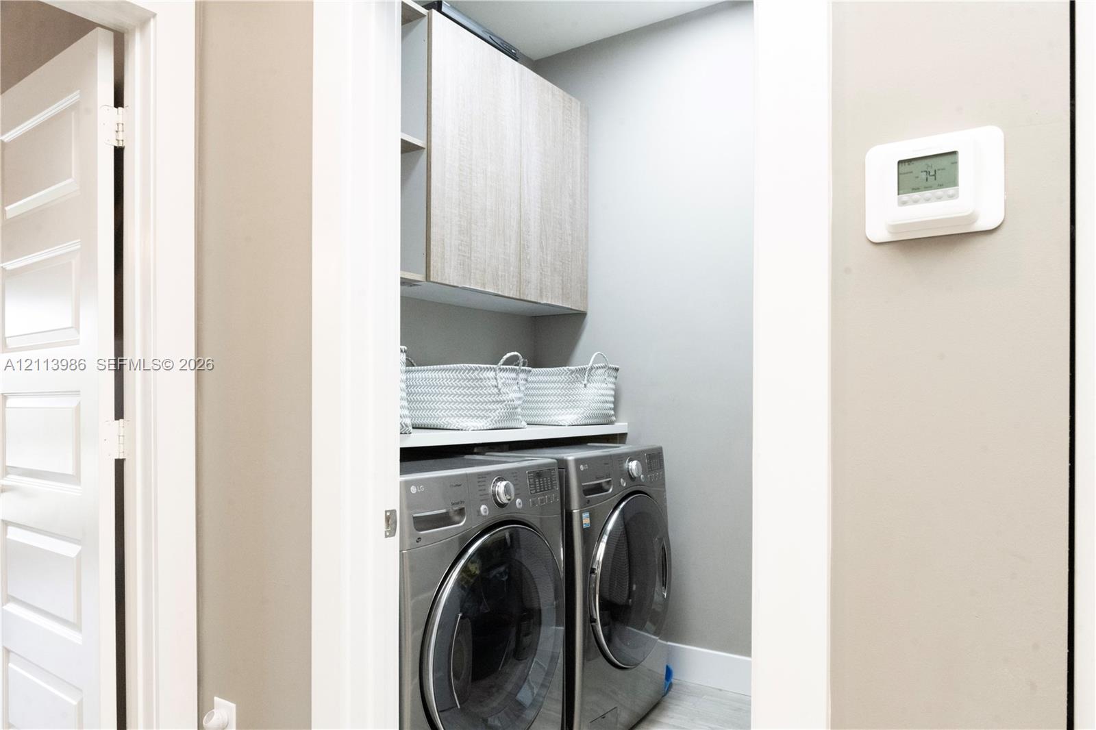 Laundry closet featuring custom wood-finish cabinetry, solid surface shelving, and a wall-mounted digital climate control thermostat