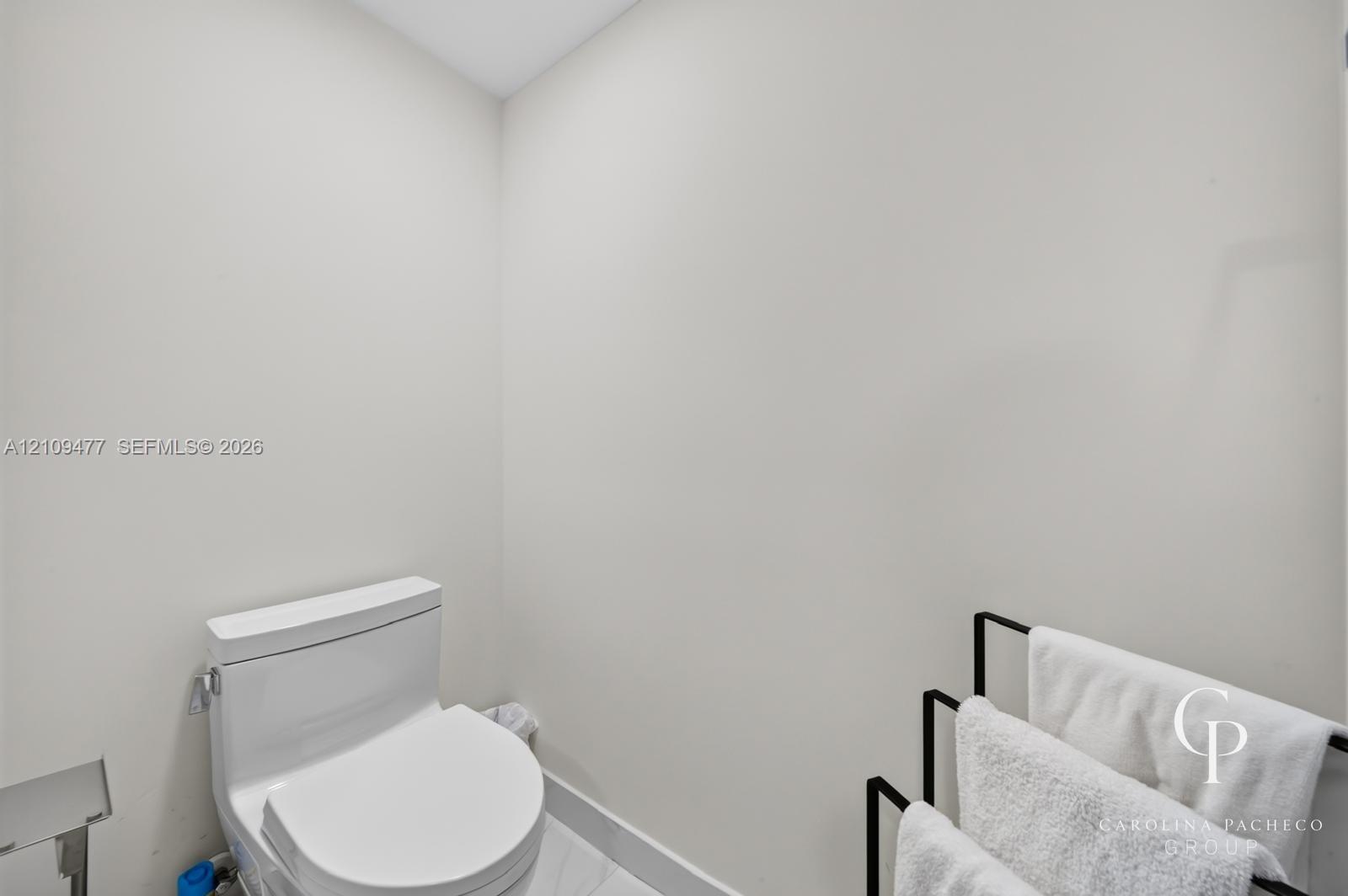 Modern white toilet with an elongated bowl and polished silver-tone hardware set against crisp neutral walls and stone-finish flooring