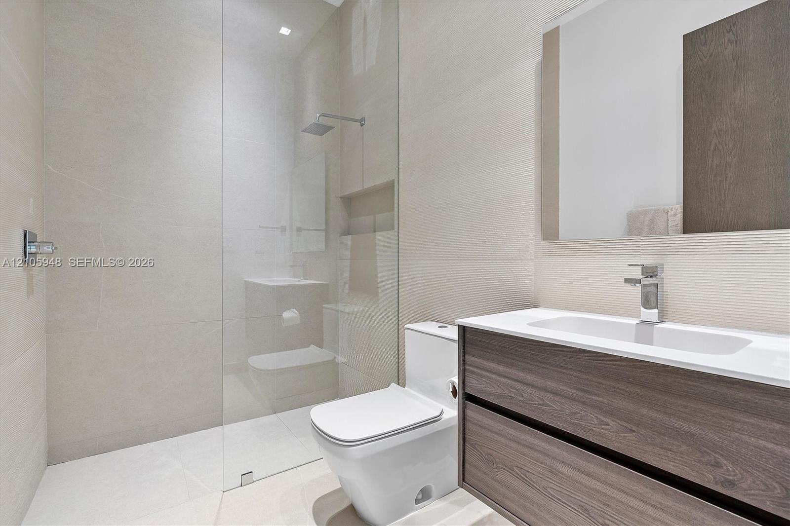 Floating vanity with wood-finish cabinetry, white countertop, integrated sink, rainfall shower head, and full-height glass shower panel