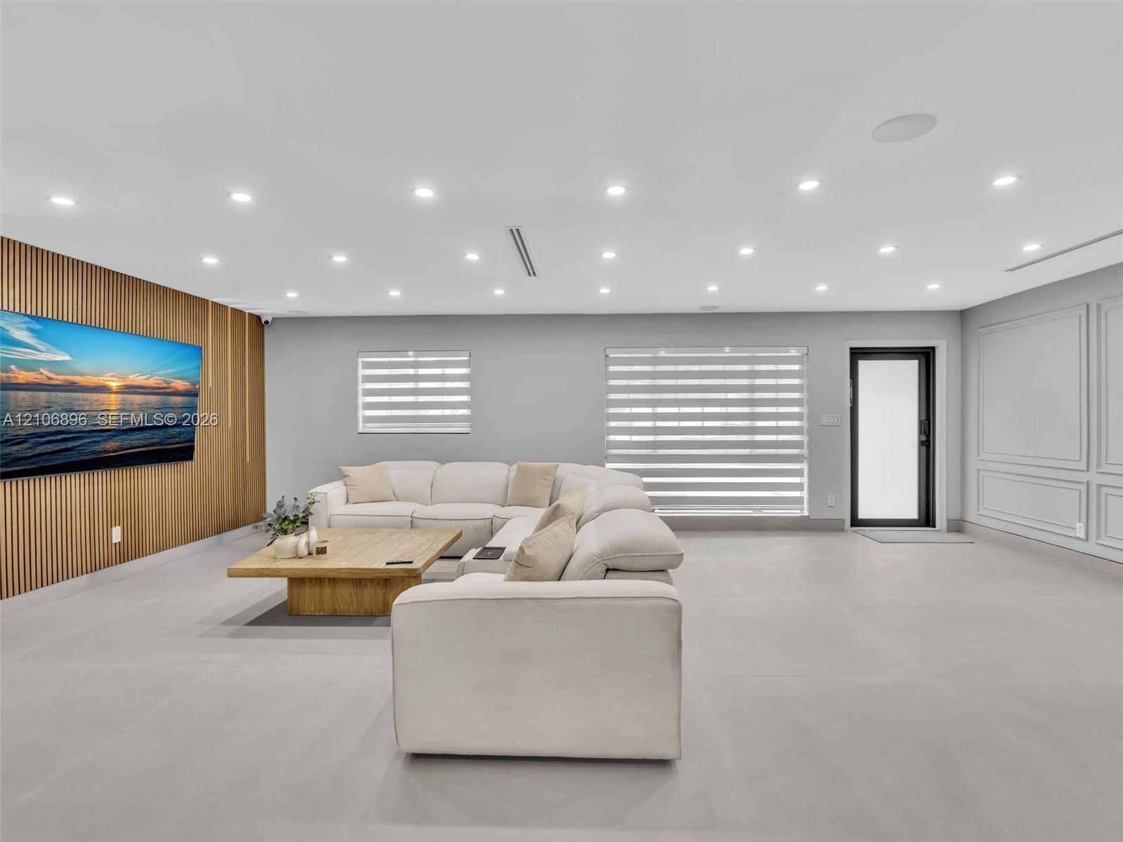 Room featuring an accent wall with vertical wood slat paneling, recessed lighting, large-format tile flooring, layered window treatments, and wainscot