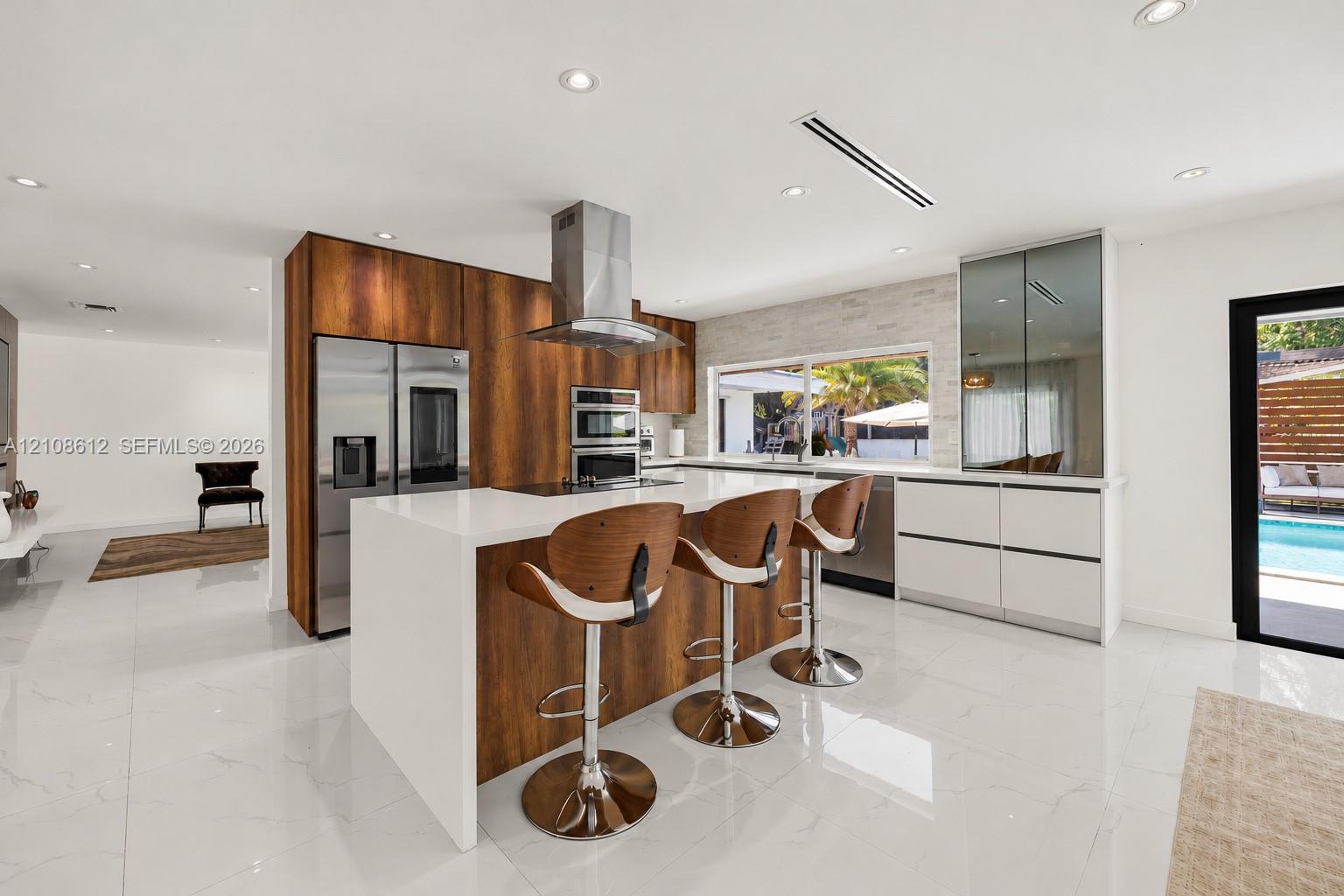Kitchen featuring custom wood-finish cabinetry, a large central island with a quartz countertop, stainless steel appliances, a stacked-stone backsplas