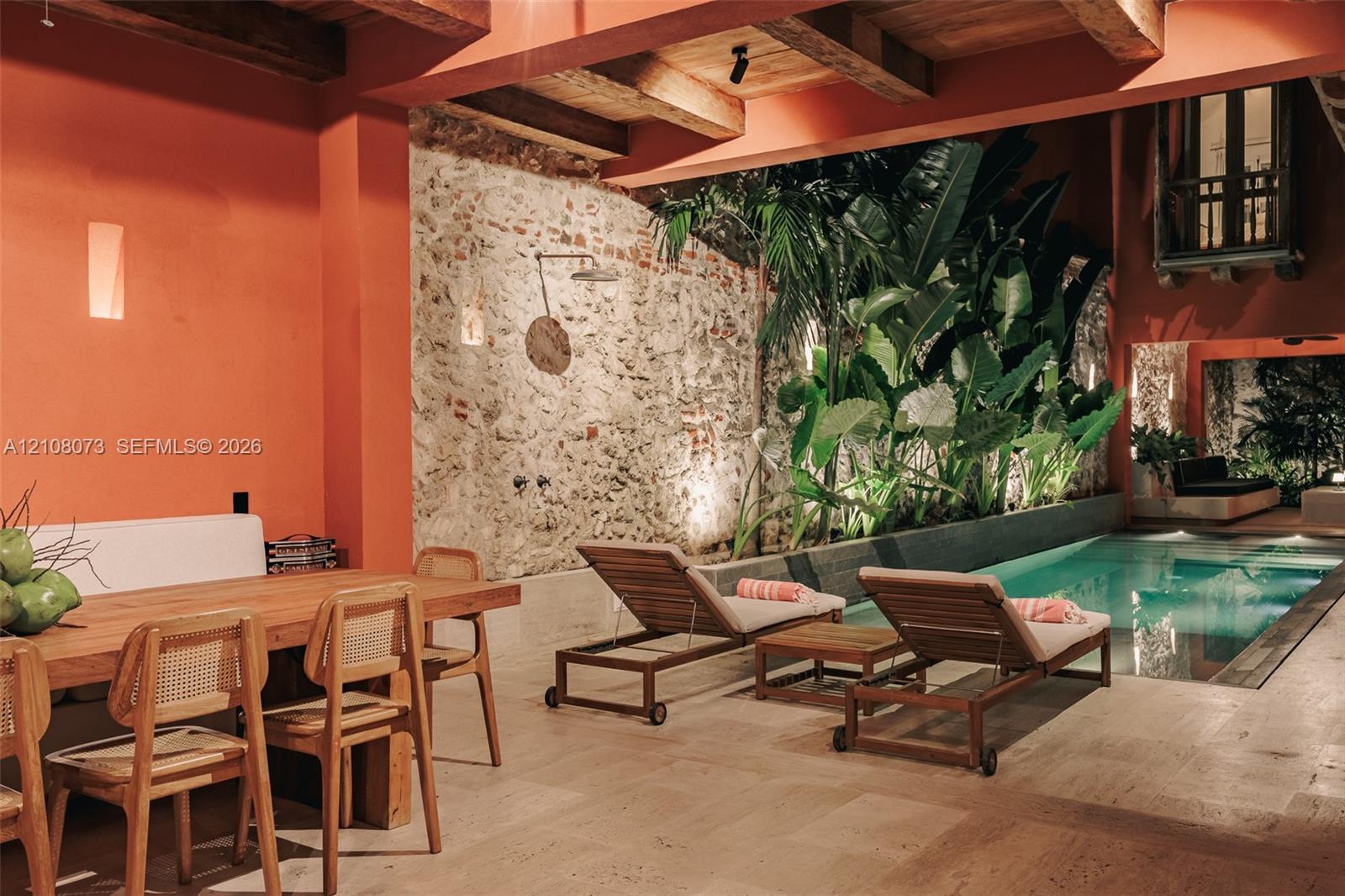 Covered patio featuring exposed timber beams, a natural stone feature wall, a wall-mounted shower fixture, and a built-in swimming pool