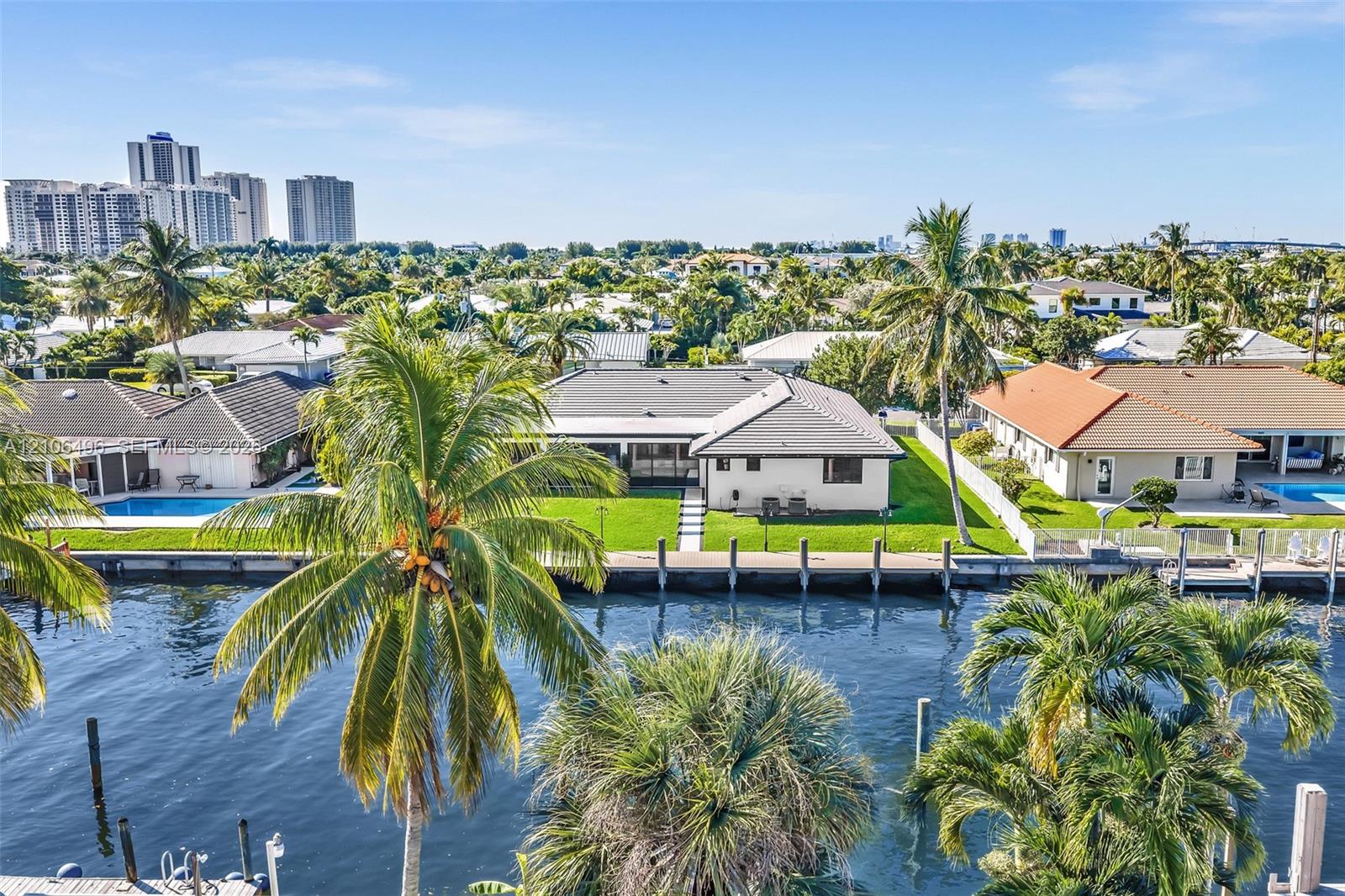 Waterfront property featuring a private seawall, manicured lawn, concrete paver walkway, and mature landscaping