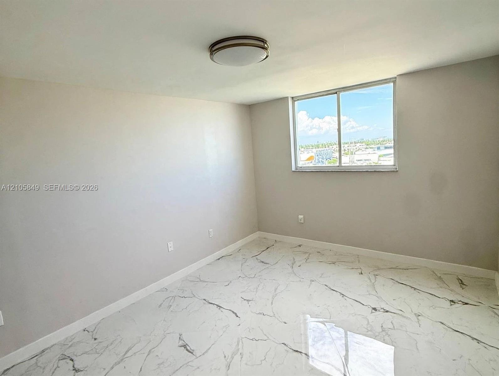 Large-format stone-style flooring with veining, neutral wall finish, and a sliding window