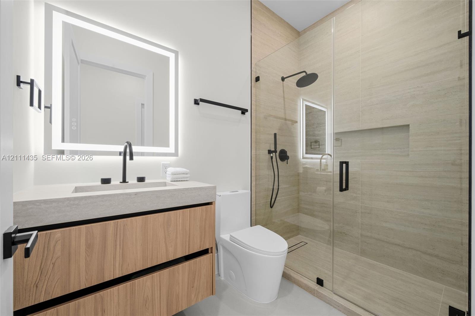 Floating wood-finish vanity with a rectangular sink, integrated LED-backlit mirror, walk-in shower with a glass enclosure and built-in recessed shelvi