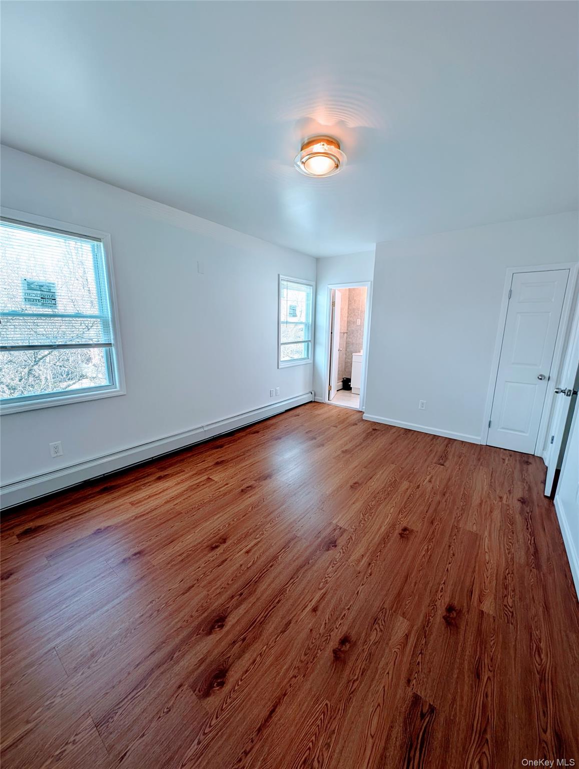 Empty room with a baseboard heating unit, baseboards, and wood finished floors
