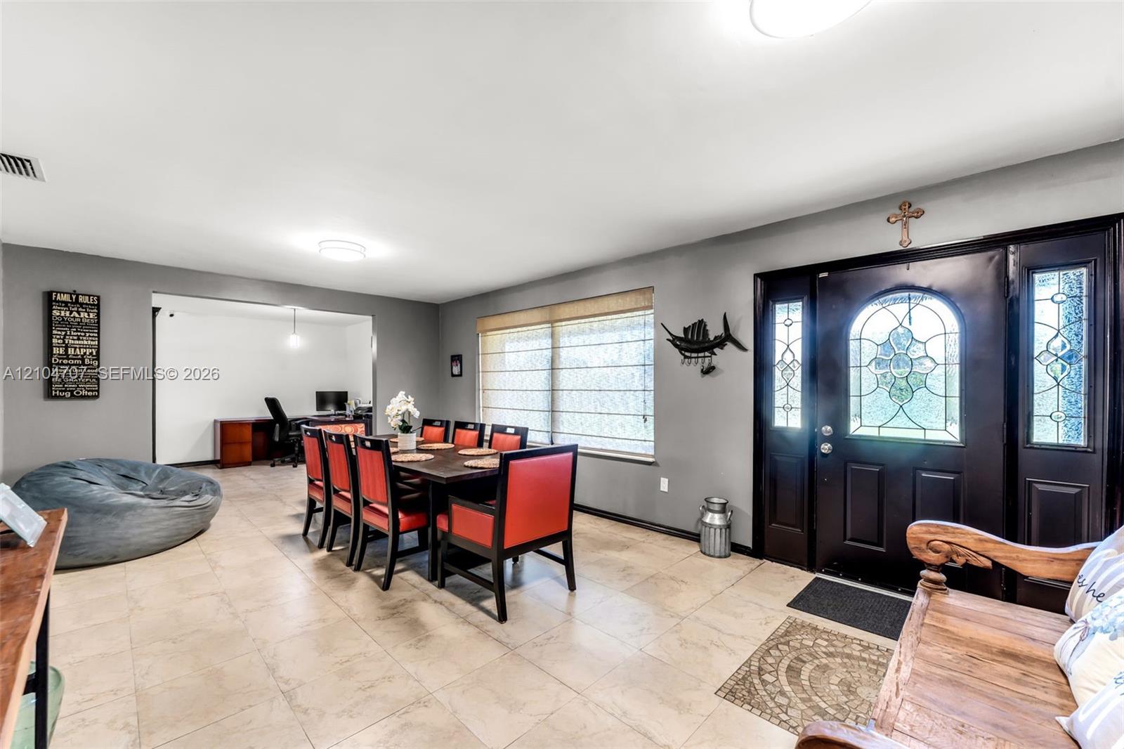 Spacious room featuring neutral tile flooring, a multi-blade ceiling fan, and large windows