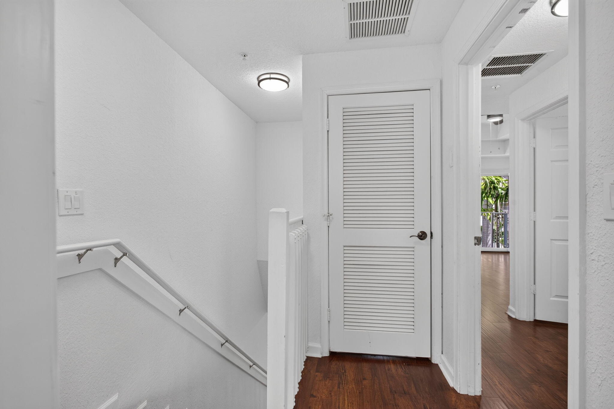 Hallway featuring wood-finish flooring, white louvered door, white painted walls, and ceiling-mounted lighting