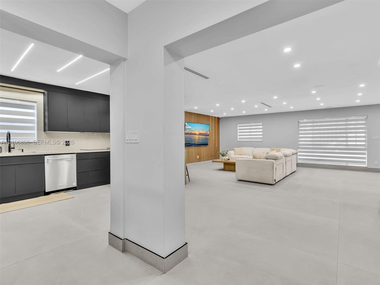 Open-concept area featuring large-format tile flooring, recessed ceiling lighting, kitchen cabinetry with a matte finish, wood-panel accent wall, and 