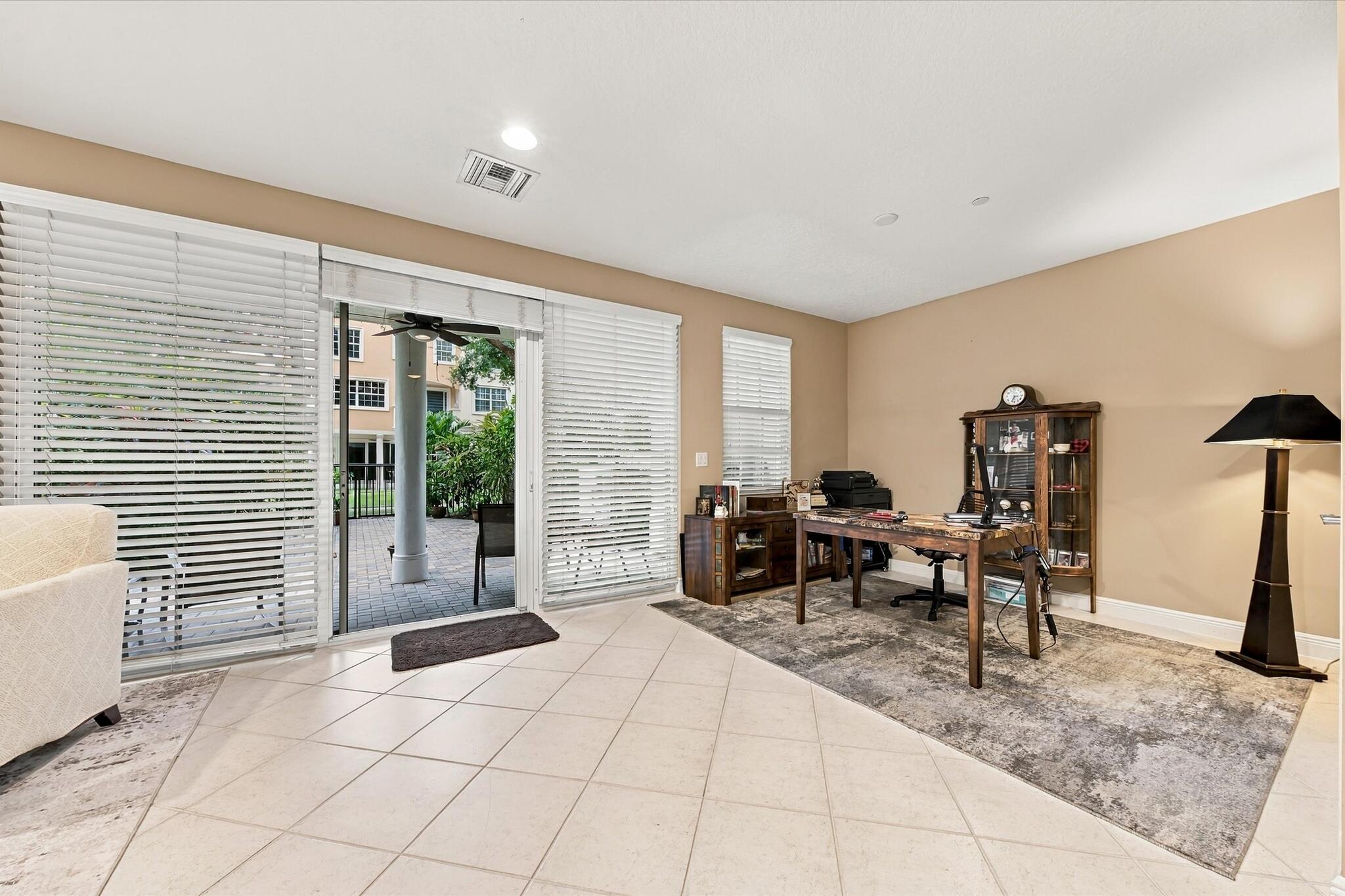 Neutral-toned interior featuring large-format tile flooring, recessed lighting, and expansive sliding glass doors with horizontal blinds, providing ac