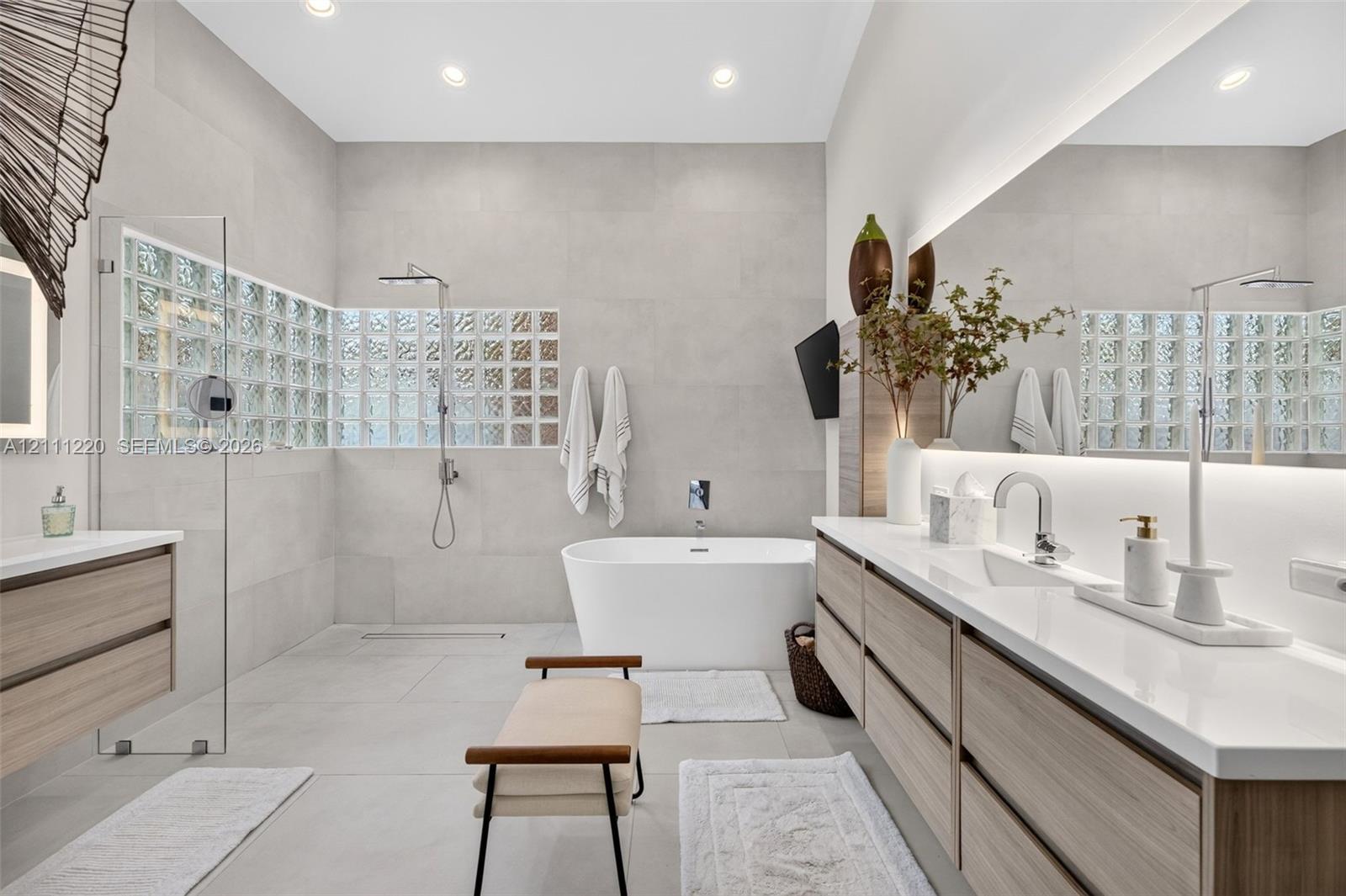 Bathroom featuring a large glass-enclosed shower, freestanding soaking tub, dual-sink vanity with light wood-finish cabinetry, quartz countertops, and
