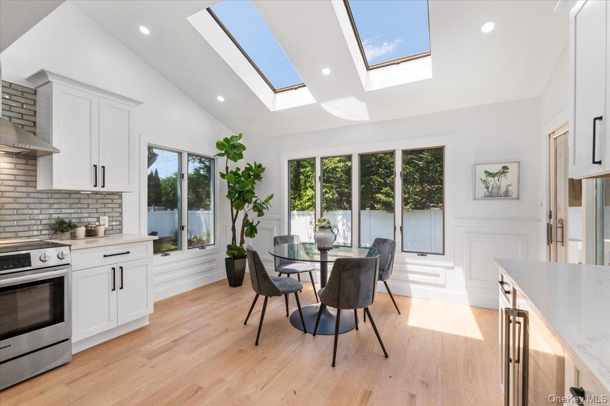 Dining room featuring a skylight, light wood-style floors, a decorative wall, a wainscoted wall, and recessed lighting