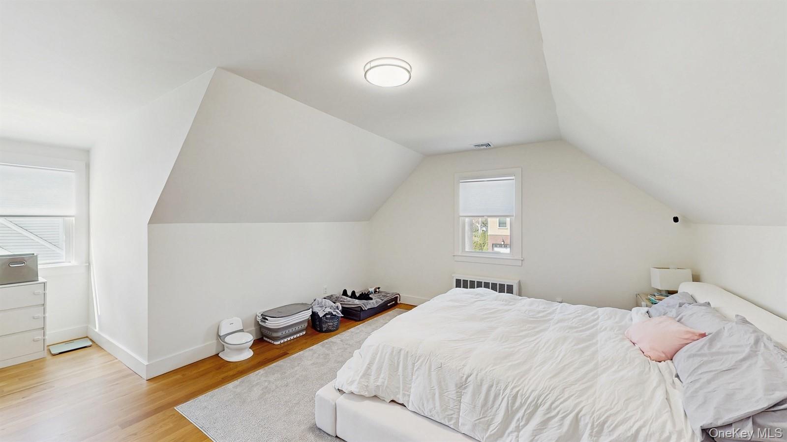 Bedroom featuring visible vents, baseboards, light wood finished floors, radiator, and lofted ceiling