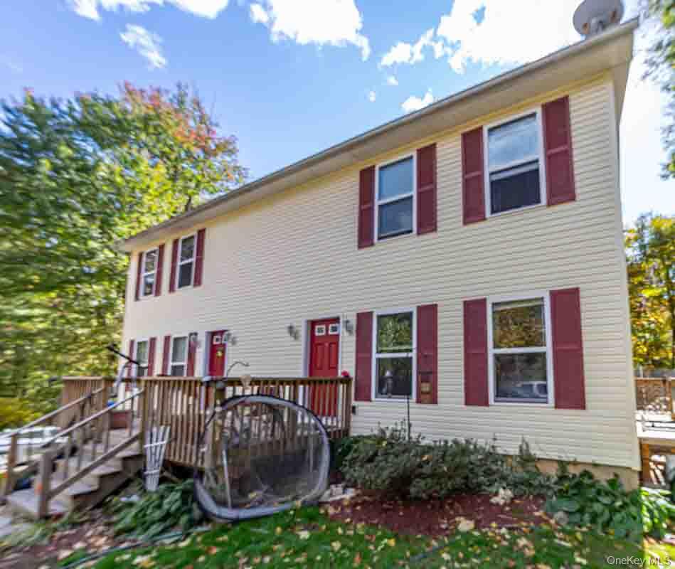 Two-story exterior with light-colored siding, multiple windows with red shutters, and a front deck with stairs