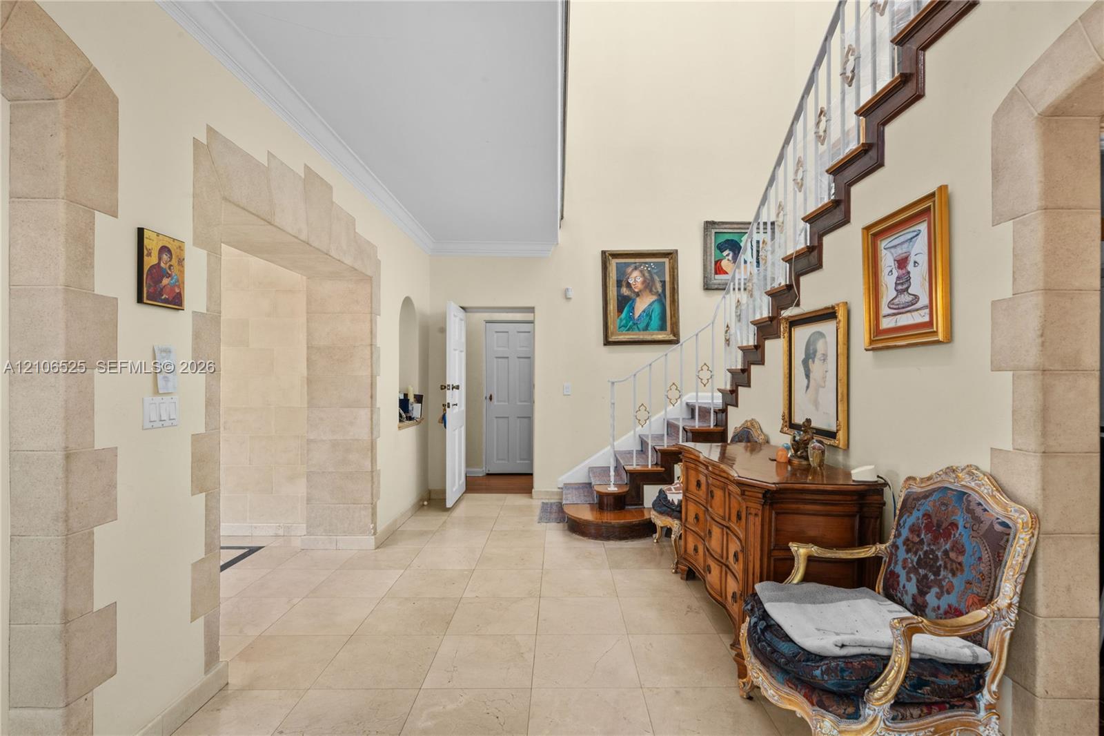 Foyer featuring high ceilings, stone-trimmed arched entryways, large-format tile flooring, and a staircase with ornate metal railings