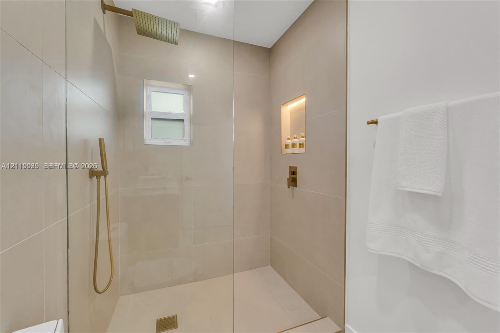 Walk-in shower featuring large-format wall tile, a frameless glass enclosure, a rainfall showerhead, a handheld sprayer in a metallic finish, and a re