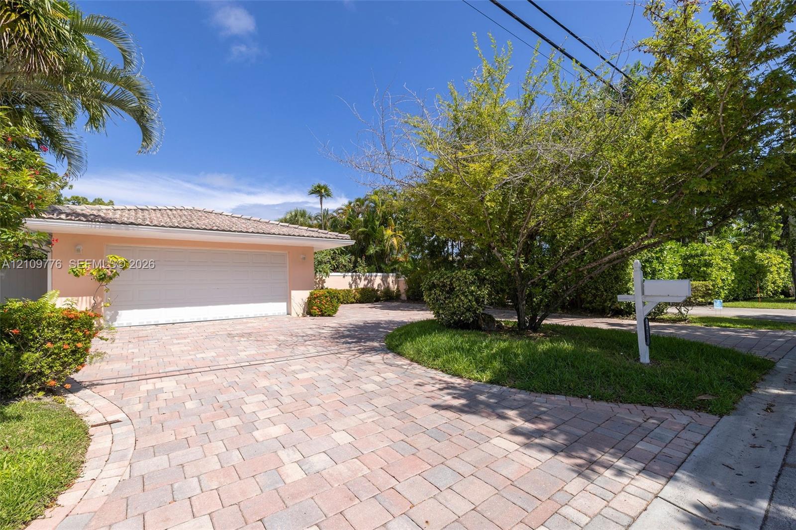 Attached two-car garage with a horizontal-panel door, expansive paver driveway, and mature landscaping