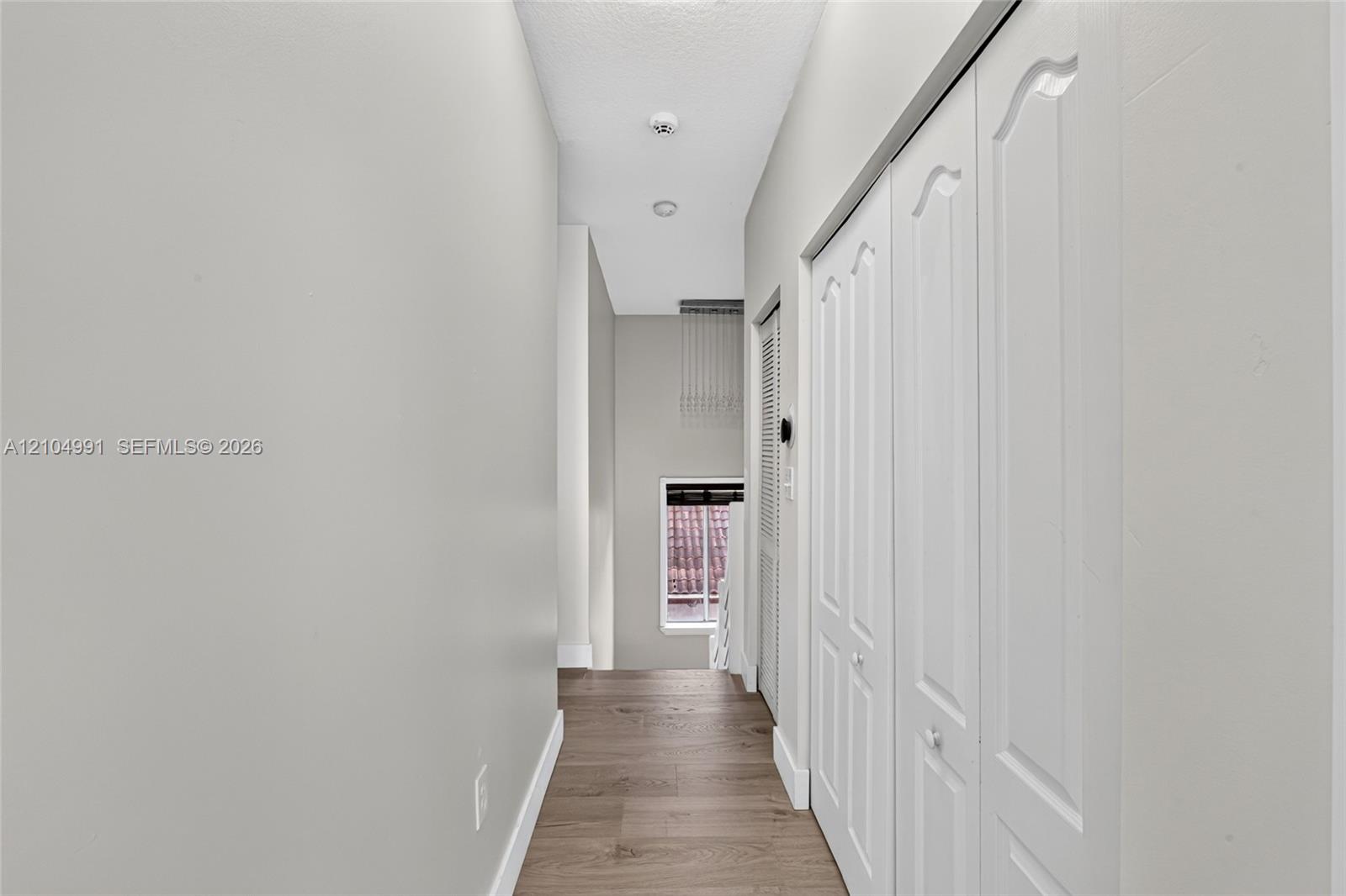 Hallway featuring wood-finish flooring, white paneled closet doors, and recessed ceiling lighting