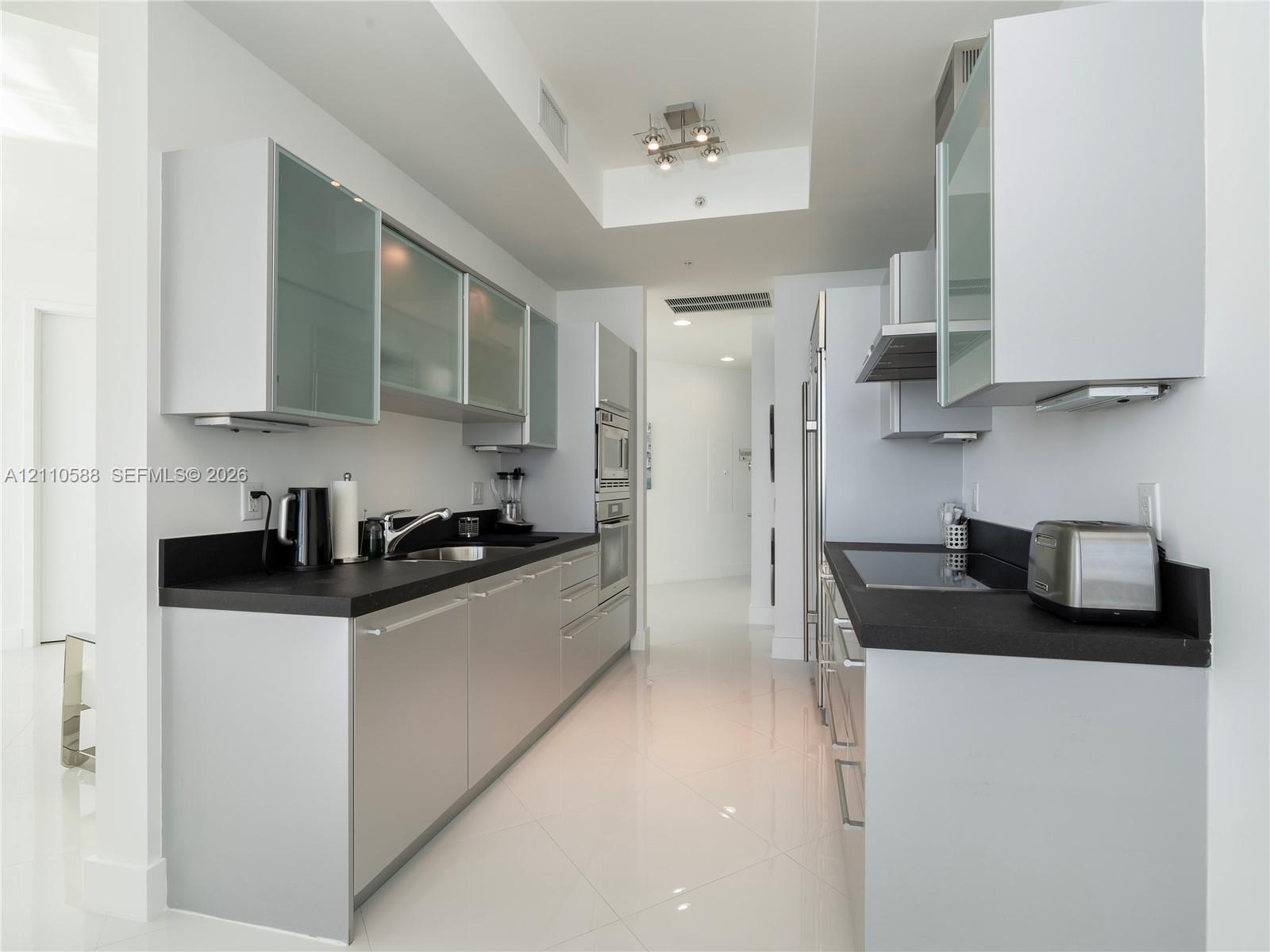 Contemporary kitchen featuring flat-panel cabinetry, frosted glass-front upper cabinets, contrasting dark countertops, integrated stainless steel appl