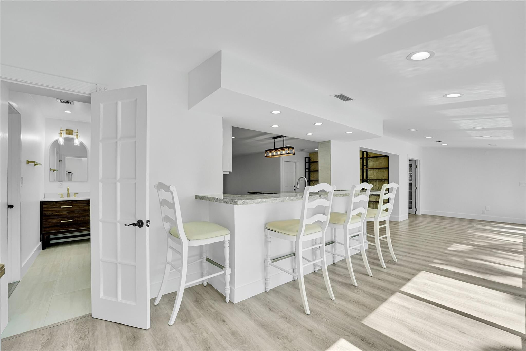 Integrated breakfast bar with a light-toned countertop, recessed lighting, wood-finish flooring, white paneled doors, and a bathroom featuring a vanit
