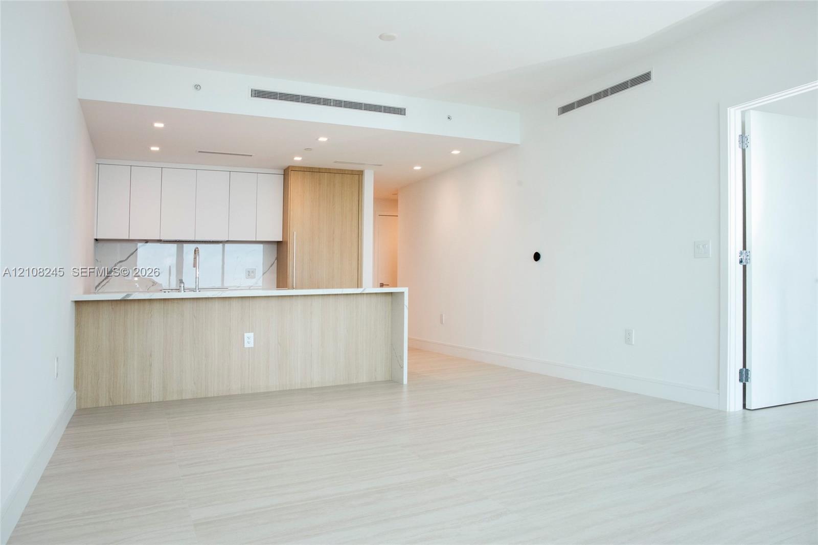 Kitchen featuring flat-panel cabinetry with wood-finish and white matte upper storage, stone-patterned backsplash, quartz countertop, and recessed cei