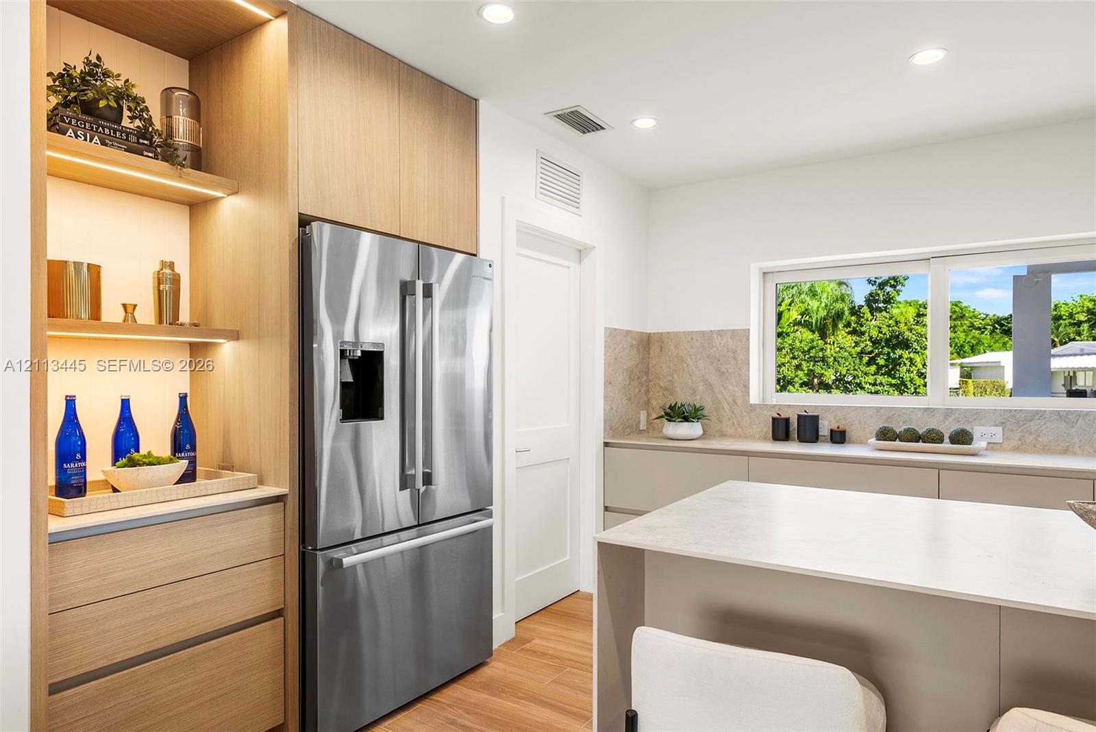 Kitchen featuring flat-panel cabinetry, light-toned stone-finish countertops, stainless steel refrigerator, integrated wood-finish shelving with reces