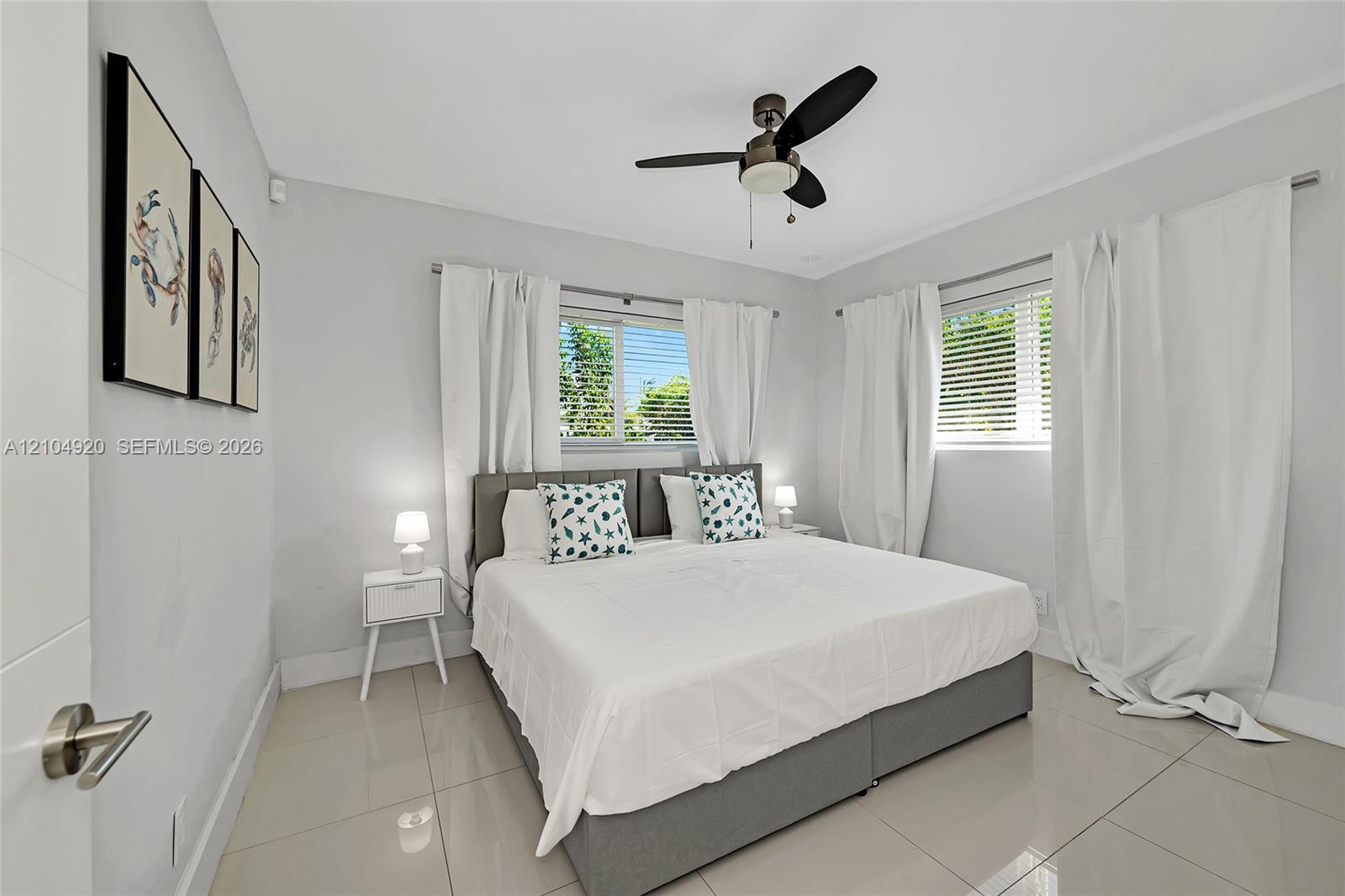 Neutral-toned interior featuring large-format tile flooring, multi-pane windows with horizontal blinds, and a central ceiling fan with integrated ligh