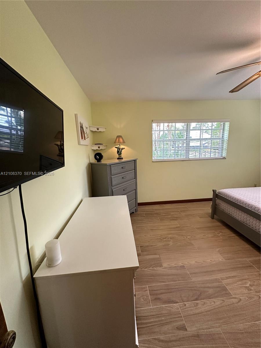 Wood-finish ceramic tile flooring, horizontal blinds, ceiling fan, and wall-mounted television bracket