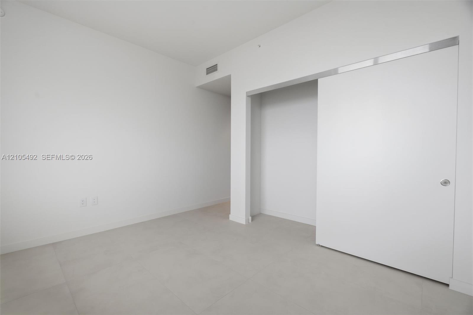 Minimalist interior featuring large-format tile flooring and a ceiling-height sliding pocket door with a metallic header track