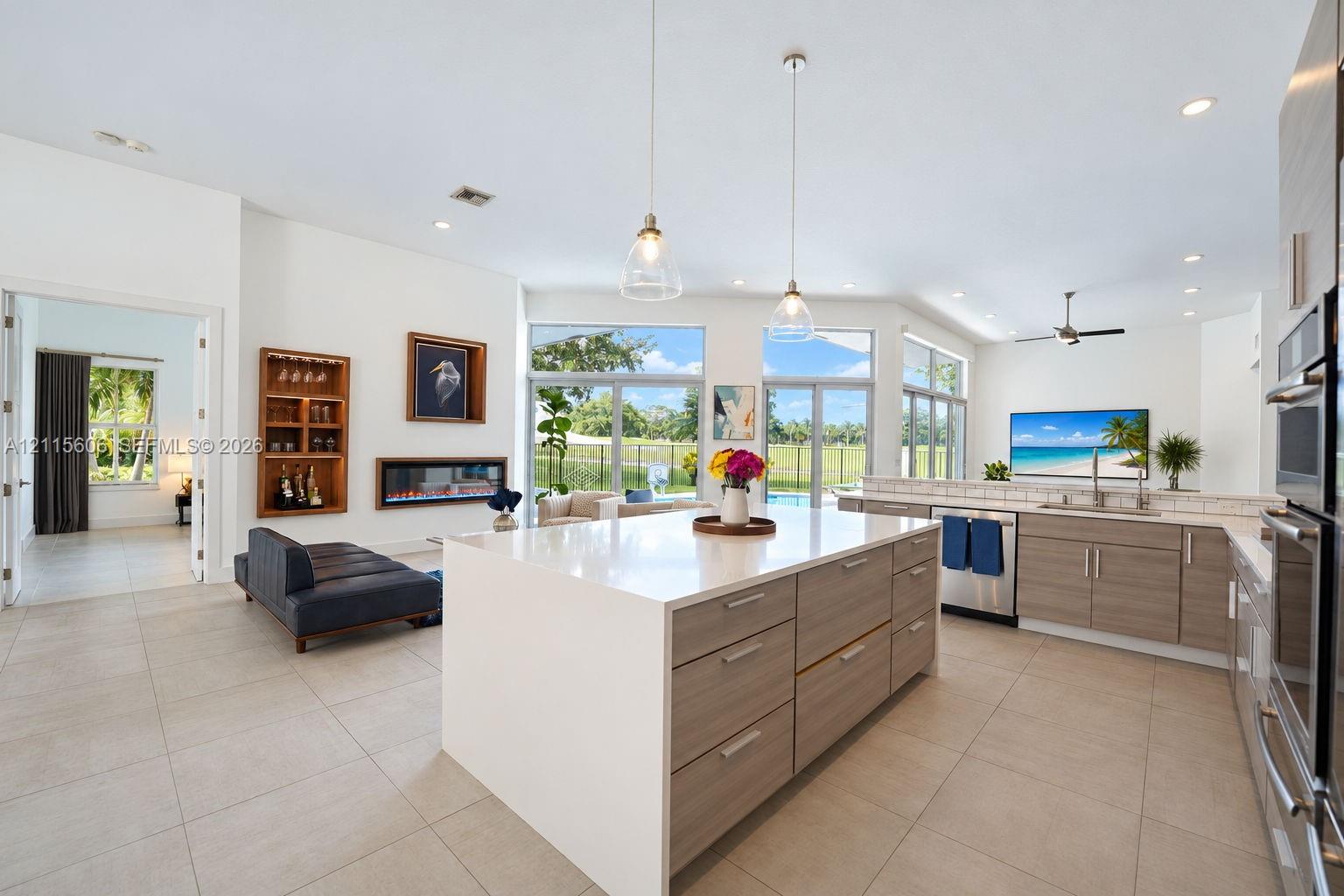 Open-concept kitchen featuring an oversized island with quartz countertops, wood-finish cabinetry, built-in stainless steel double ovens, recessed lig
