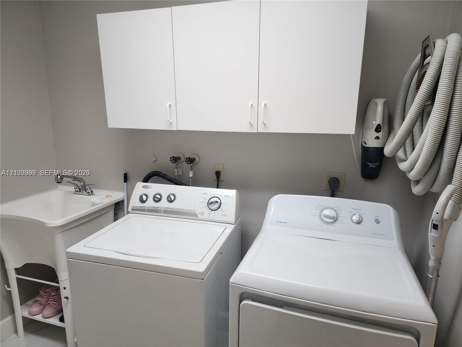 Utility room featuring white cabinetry, a freestanding basin with a chrome faucet, and integrated laundry hookups