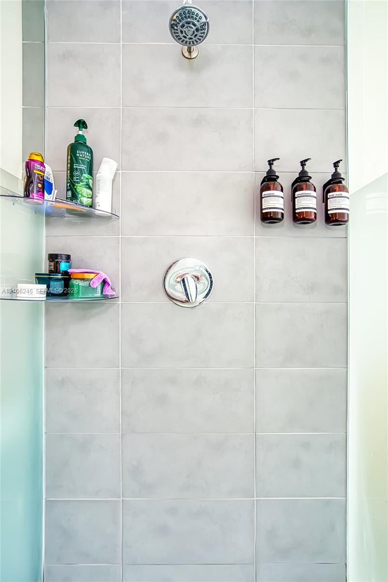 Shower stall featuring large-format light gray tile, a chrome rainfall showerhead, a single-handle chrome pressure balance valve, and two integrated g