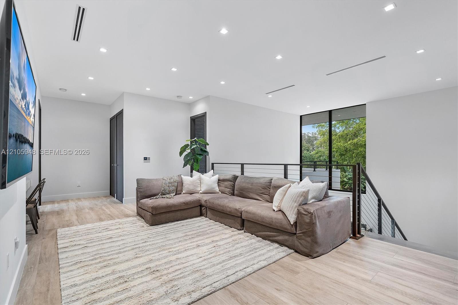Open-concept space featuring light wood-finish flooring, recessed ceiling lighting, linear HVAC diffusers, and a staircase with a horizontal cable rai