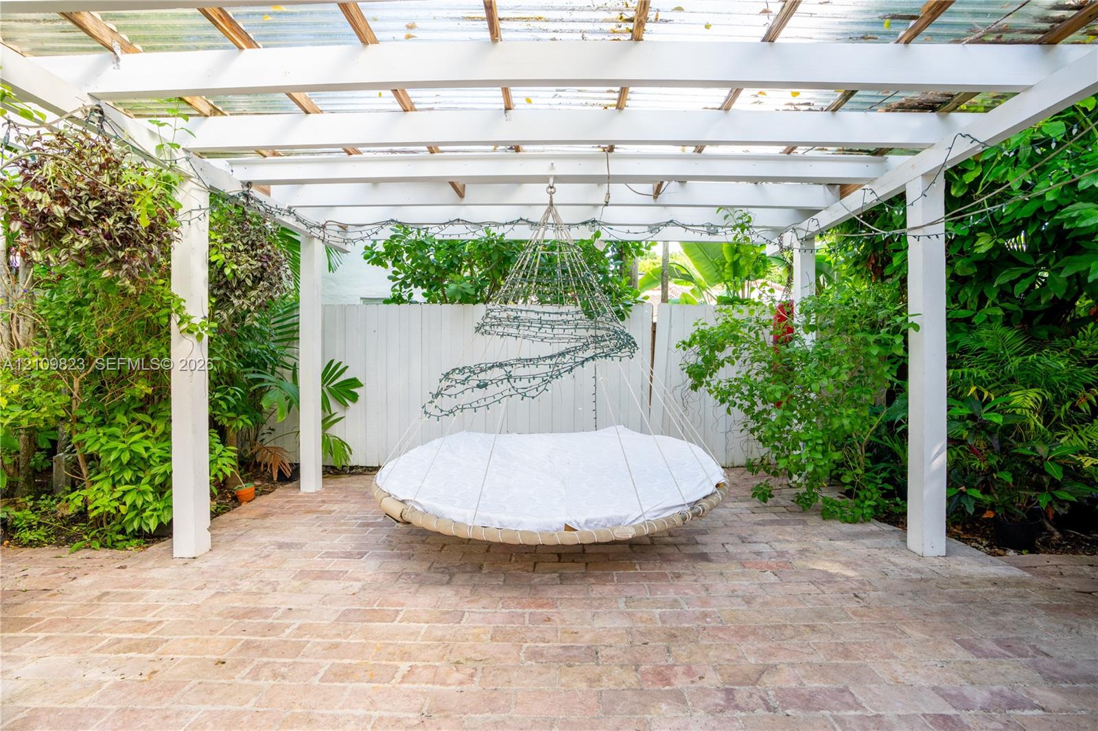 Outdoor patio featuring a white pergola structure, paver flooring, and privacy fencing