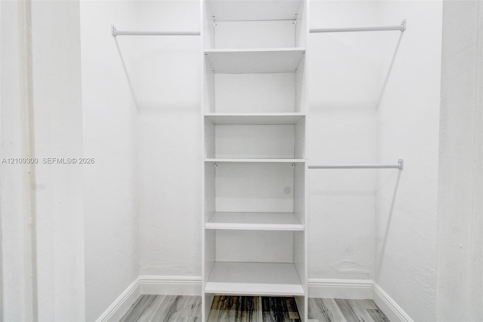 Walk-in closet featuring white built-in shelving, dual-level garment rods, and wood-finish flooring