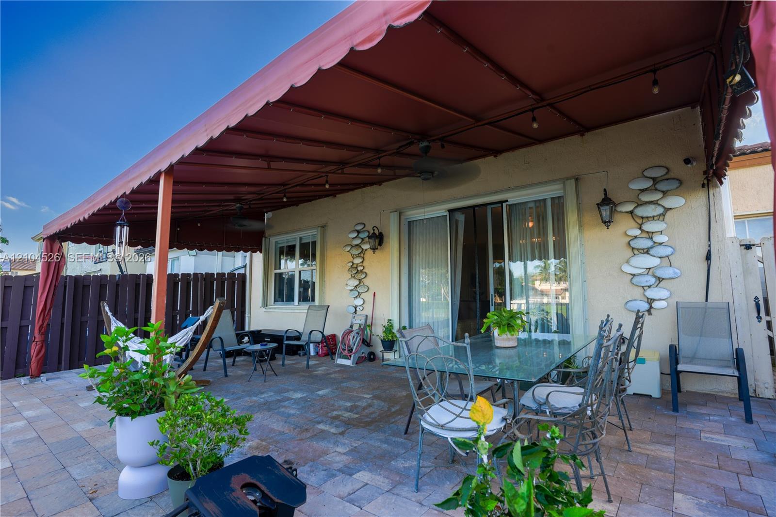 Covered outdoor patio featuring paver flooring, a retractable fabric awning, dual ceiling fans, and wall-mounted exterior light fixtures