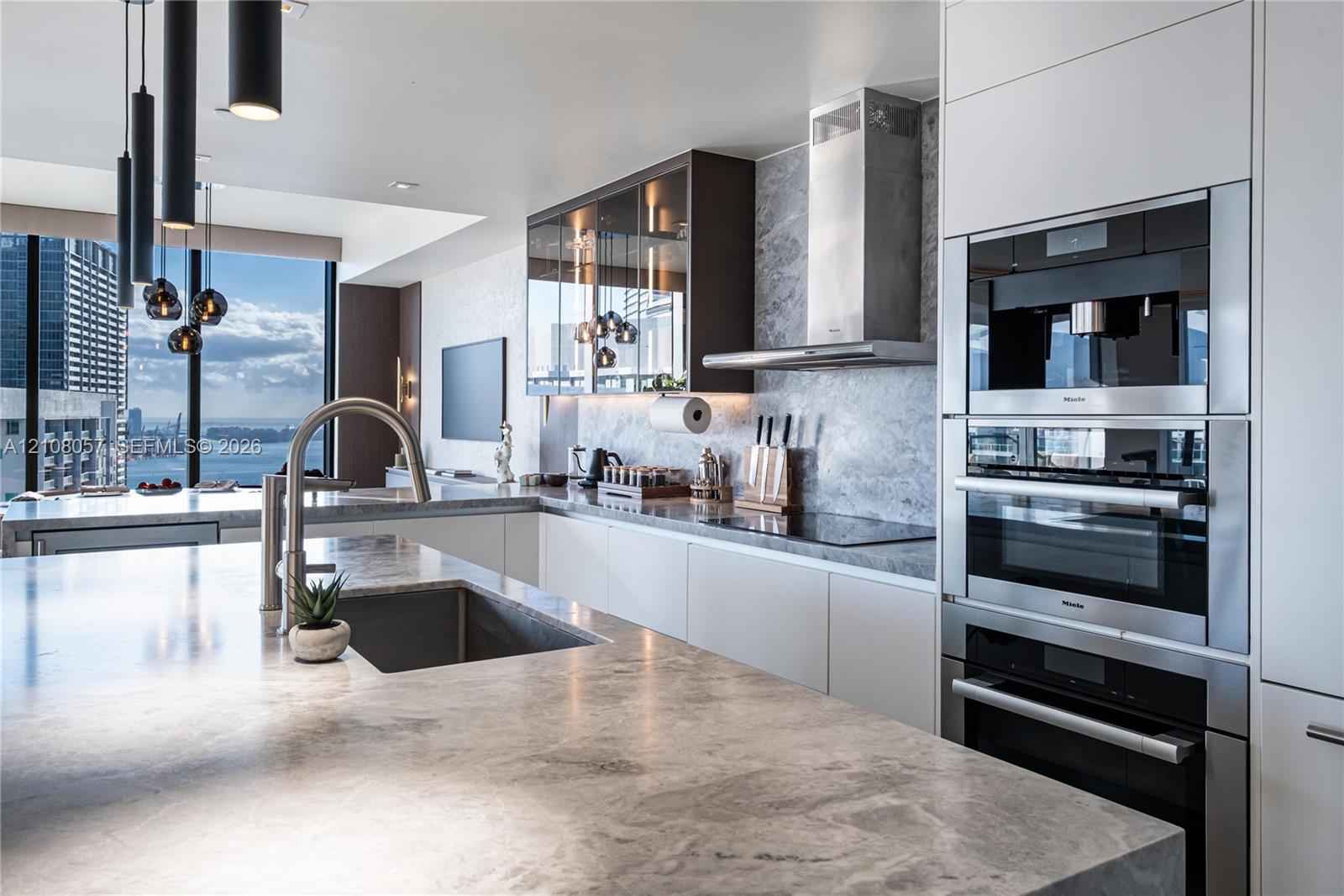 Contemporary kitchen featuring stone countertops, integrated stainless steel appliances, matte-finish flat-panel cabinetry, glass-front upper storage,