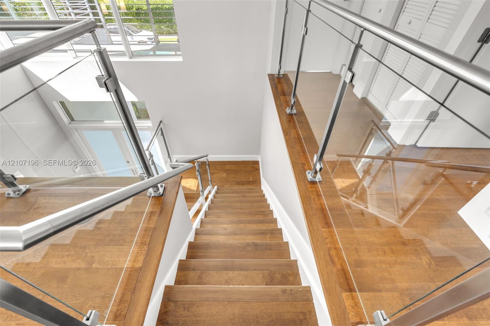 Staircase featuring wood-finish flooring, stainless steel handrails, and glass panel balustrades