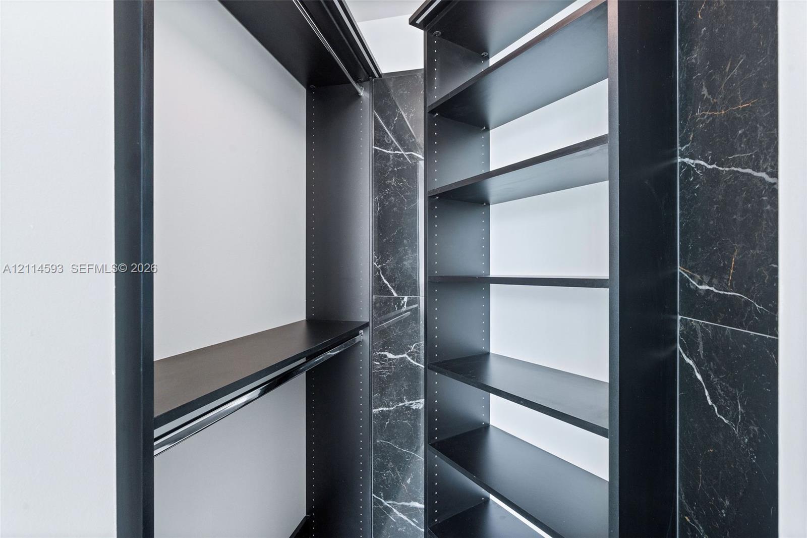 Built-in closet organization featuring matte black shelving, hanging rods, and dark stone-patterned wall surfacing