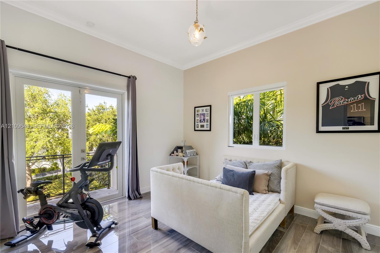 Room featuring wood-finish tile flooring, crown molding, glass-paned French doors opening to a balcony with decorative railing, and a pendant light fi