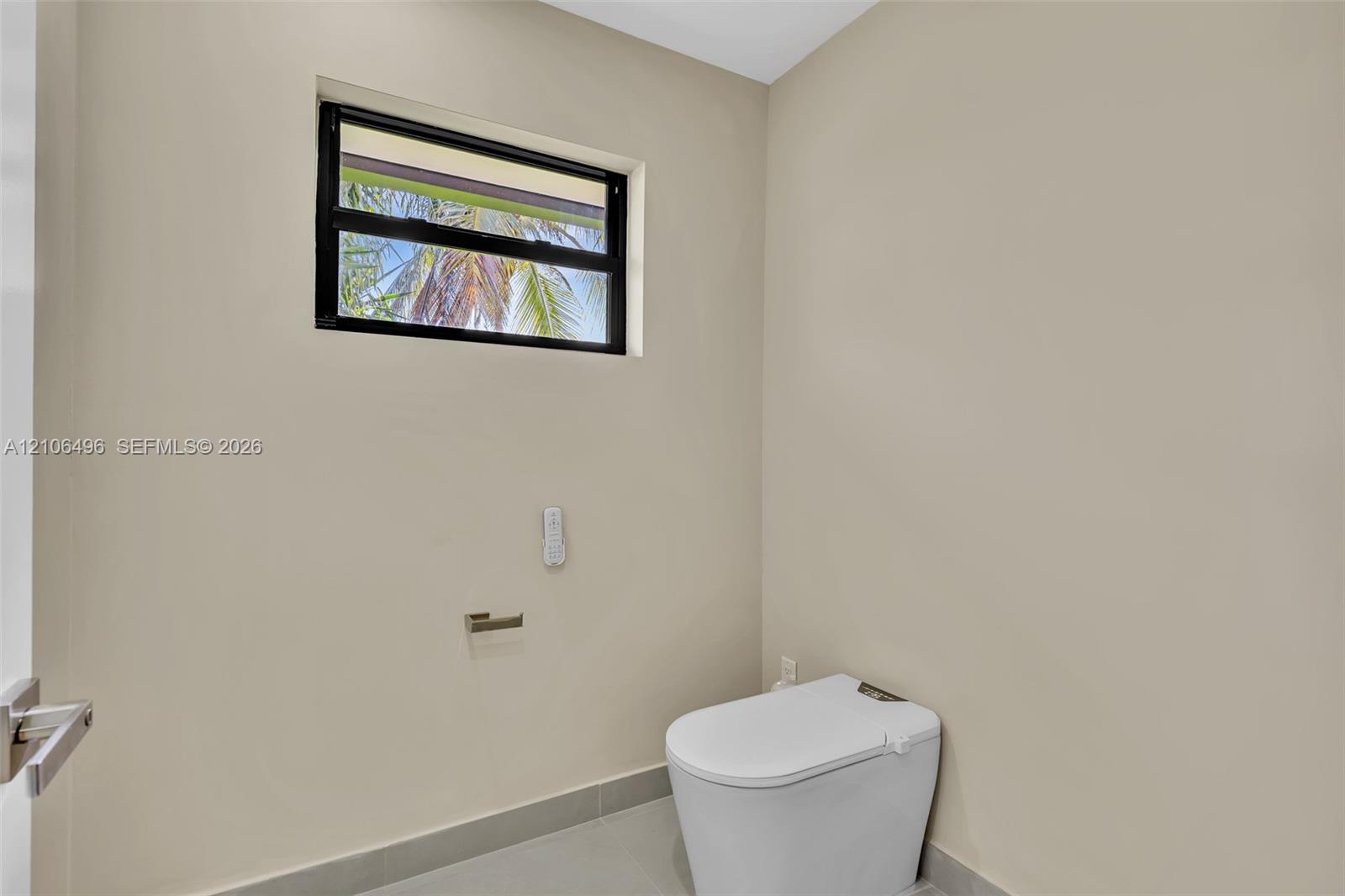 High-profile window with black frame, wall-mounted toilet, and sleek metal toilet paper holder
