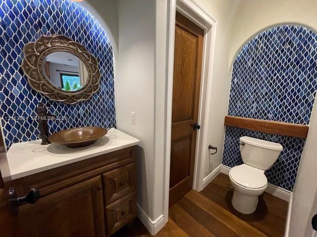 Custom vanity with stone countertop and copper vessel sink, arched alcoves with blue patterned tile work, wood-finish flooring, and solid wood interio