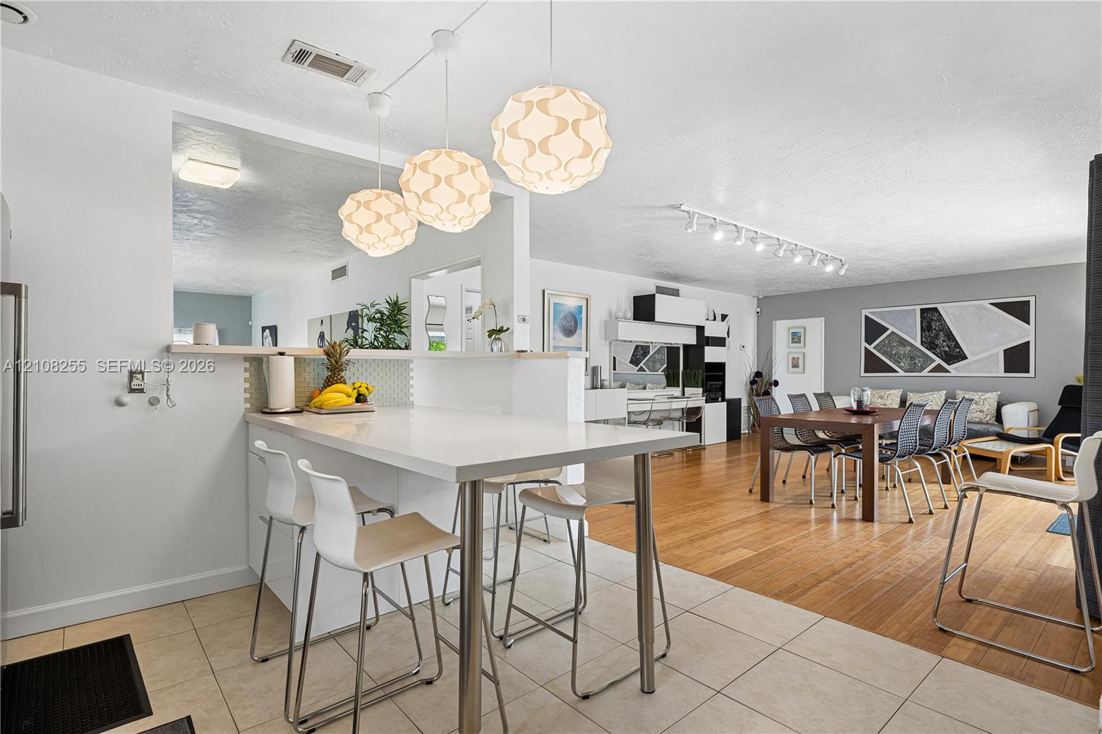 Kitchen peninsula with a solid-surface countertop and integrated breakfast bar, complemented by three spherical pendant light fixtures, large-format t