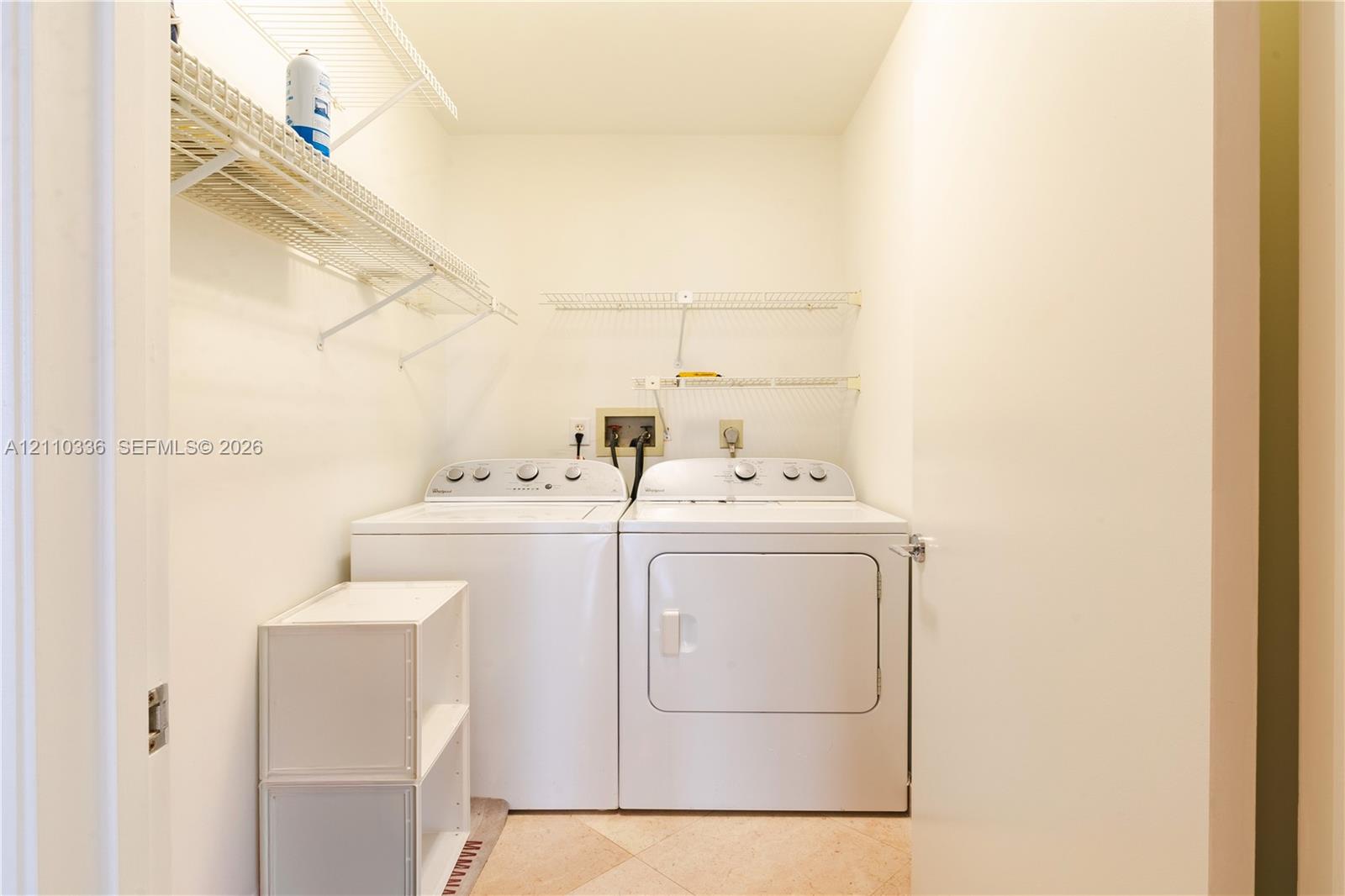 Utility area featuring white metal wire shelving and neutral-toned tile flooring