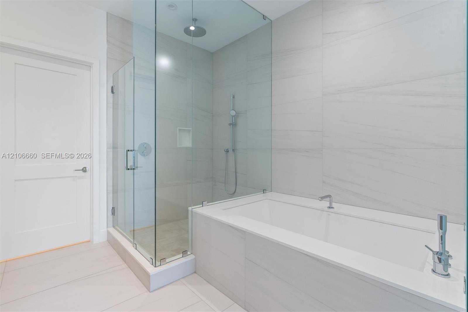 Walk-in glass-enclosed shower featuring a rainfall showerhead, integrated tiled wall niche, deep soaking tub with deck-mounted faucet, and large-forma